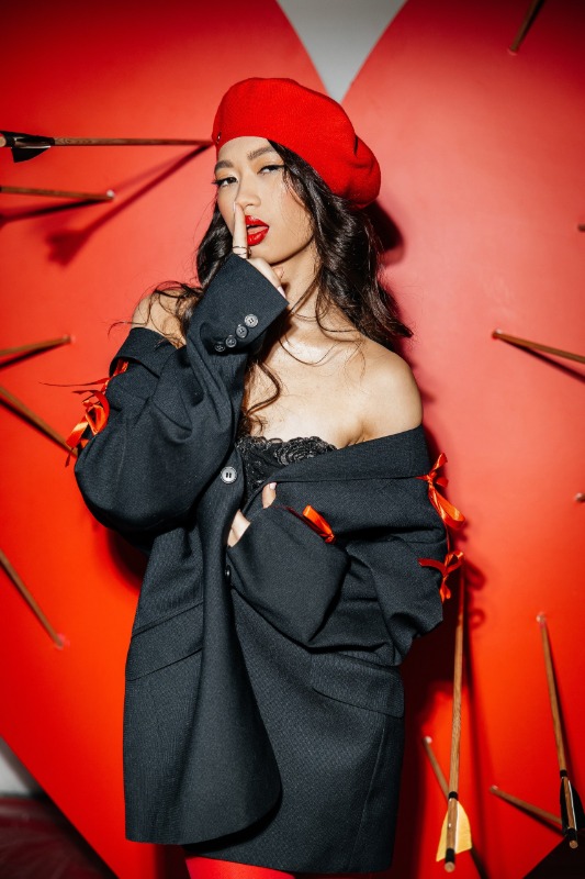 Женщина в красном берете и черном пиджаке на фоне красной стены с декоративными стрелами