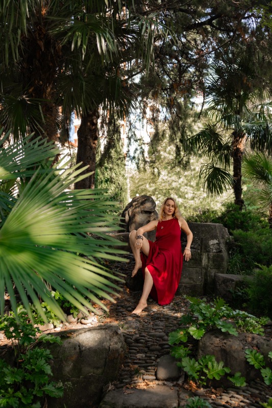 Женщина в красном платье позирует среди тропических растений на каменных ступенях в саду